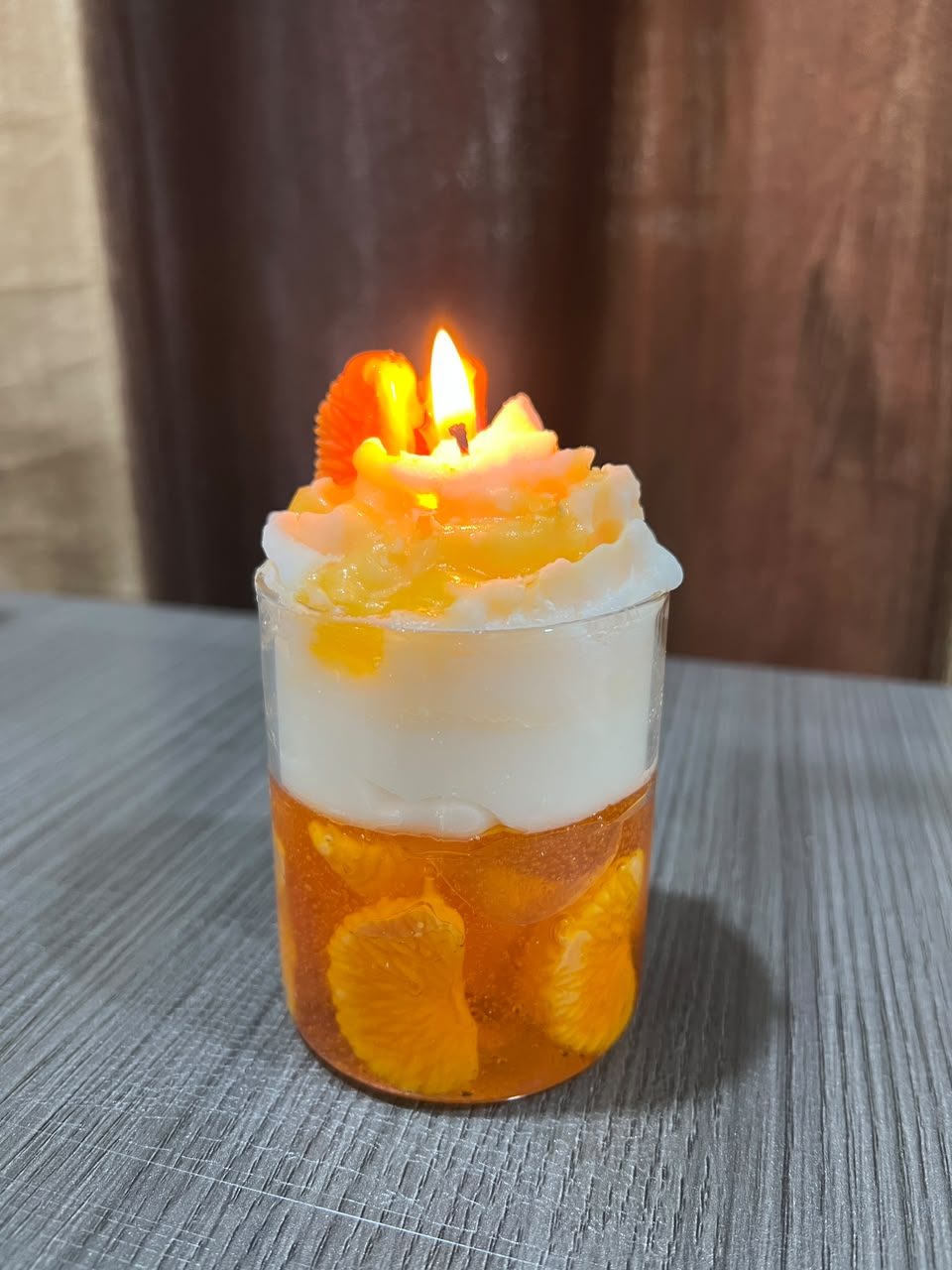 A customer's Pairsense Orange candle lit, its whipped wax top over orange segments in amber gel